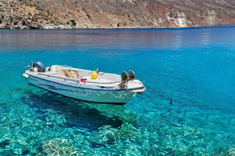 Un pequeño barco sobre agua clara frente a la costa cretense